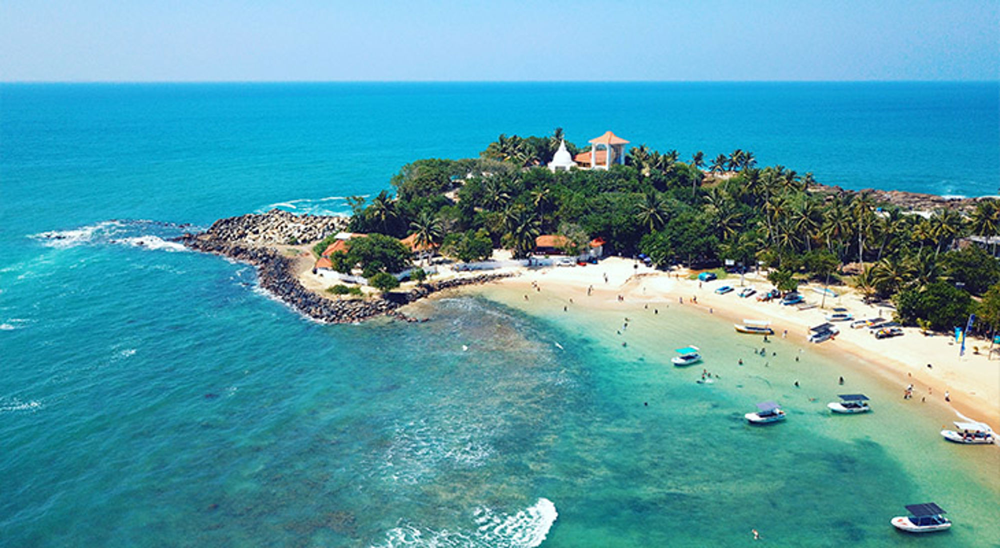 Unawatuna Sri Lanka een tropisch strand met palmbomen, bootjes en helderblauw water.
