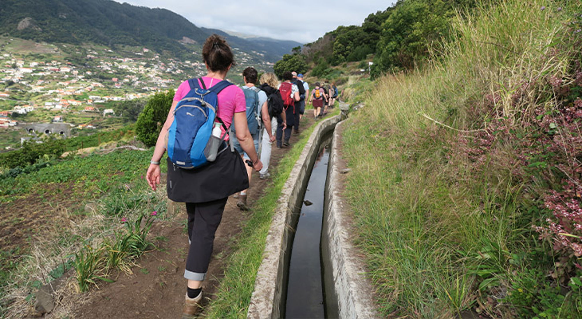 Groep wandelaars met rugzakken op een bergpad langs een irrigatiekanaal tijdens een wandelvakantie met Sawadee.