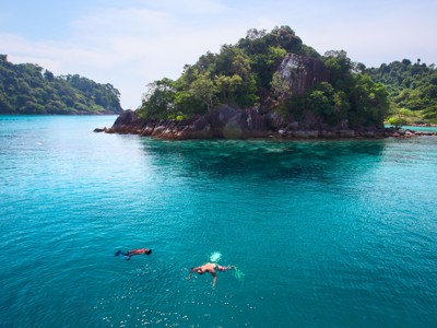 Snorkelaars in helderblauw water bij een groen eiland voor de kust van Zuid-Thailand.