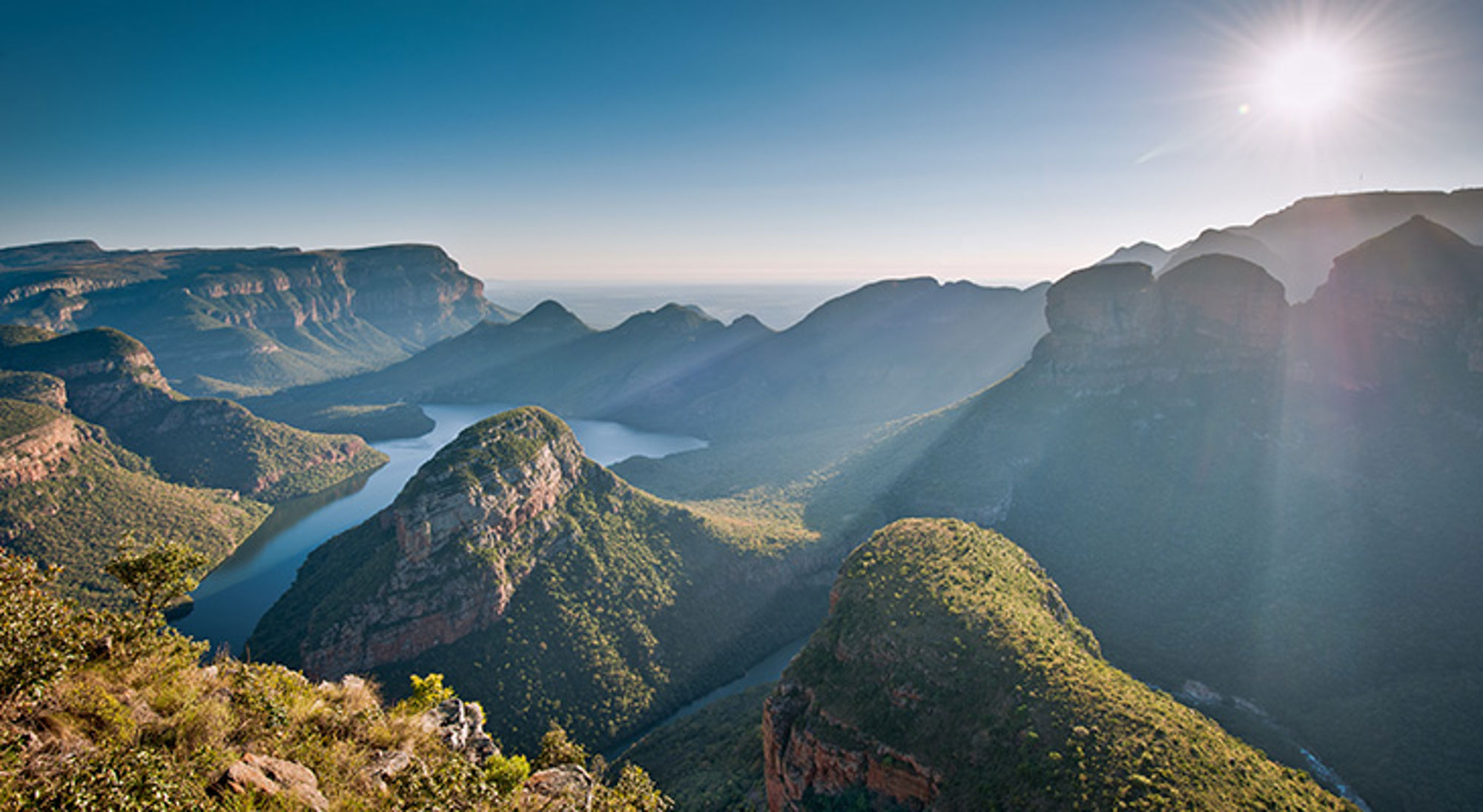 Panorama van de Blyde River Canyon met kronkelende rivier en bergen in Zuid-Afrika bij zonlicht.