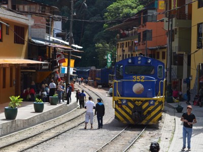 Blauwe trein op de spoorlijn door Aguas Calientes, Peru, met reizigers langs de rails.