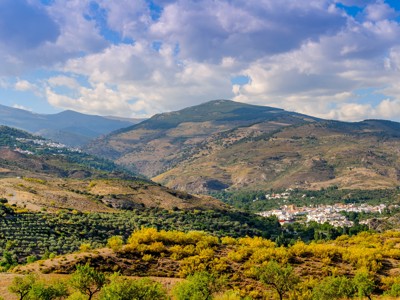 Panorama op de Sierra Nevada met bergdorp in de vallei en glooiende heuvels onder een wolkenlucht.