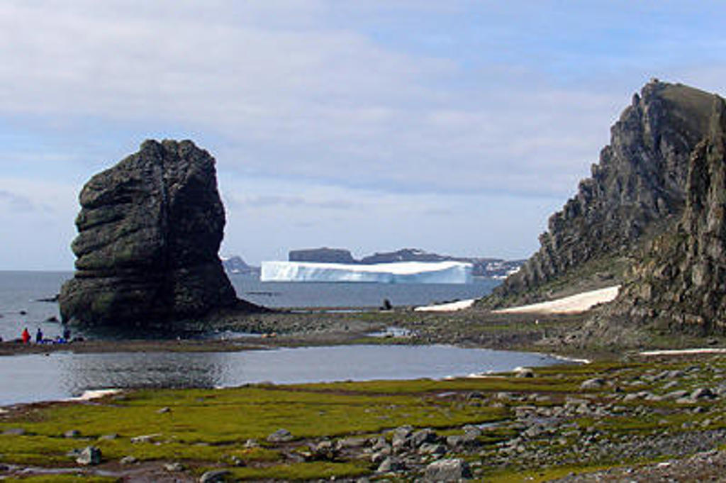 Rotsachtige kust in Antarctica met ijsberg op zee, tijdens de expeditie Crossing the Circle voorbij de Zuidpoolcirkel.