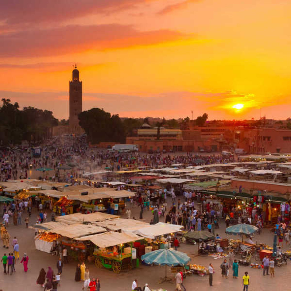 Zonsondergang boven het Djemaa el Fna-plein in Marrakech, met marktstalletjes en de Koutoubia-minaret.