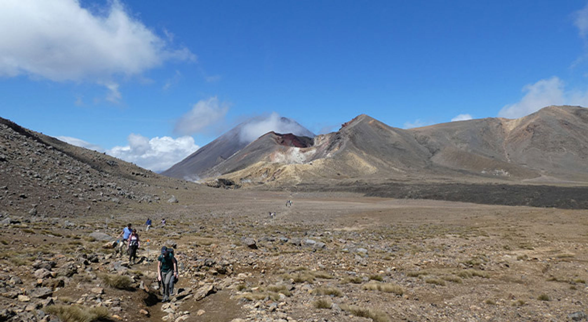 Central Crater Wandelaars op een ruig bergpad met vulkaanlandschap onder een heldere blauwe lucht.