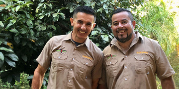 Twee lokale gidsen en chauffeurs in Costa Rica dragen nieuwe Sawadee-uniforms en lachen in het groen.