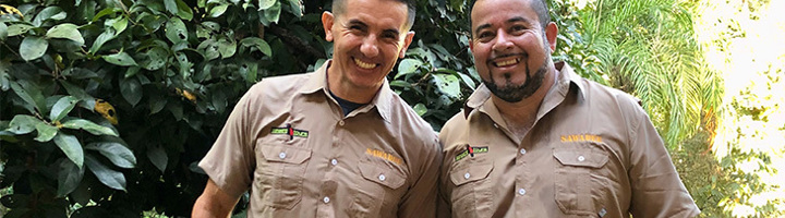 Twee lokale gidsen en chauffeurs in Costa Rica dragen nieuwe Sawadee-uniforms en lachen in het groen.