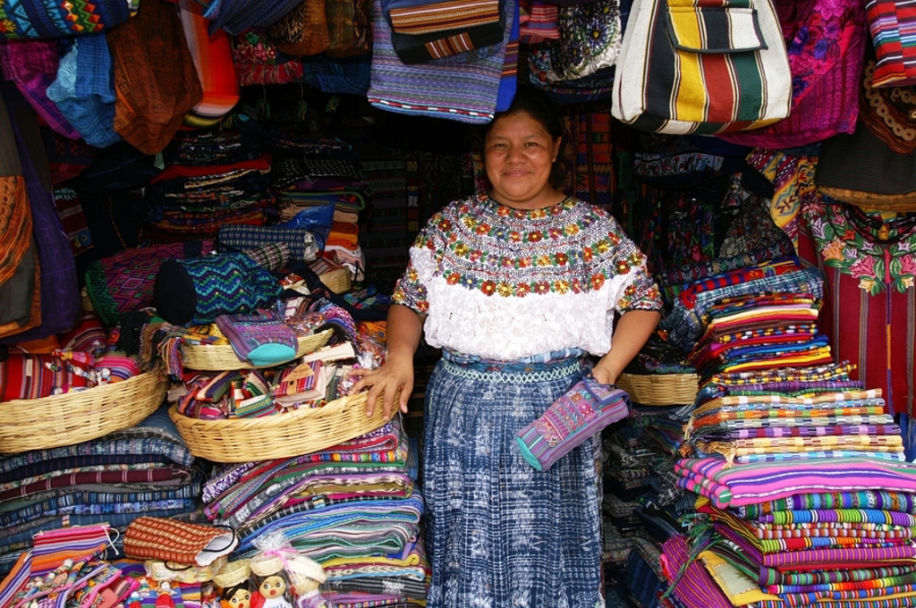 Vrouw bij marktstalletje met kleurrijke geweven textiel en handwerk in Guatemala tijdens groepsrondreis Guatemala en Copán.