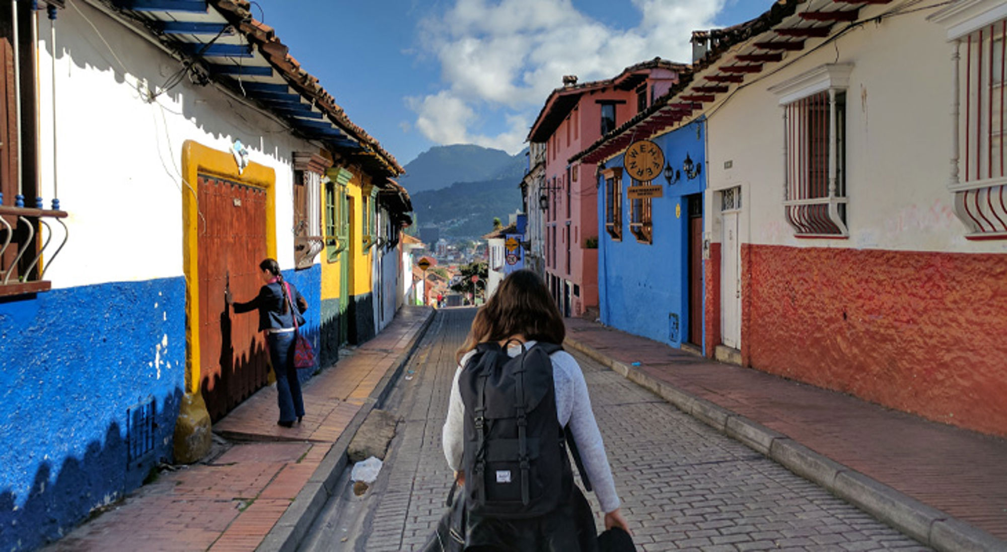Kleurrijke huizen La Candelaria Backpacker loopt door kleurrijke straat in Bogotá, Colombia, met bergen op de achtergrond.