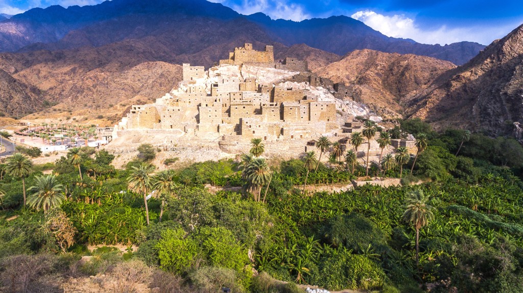 Traditioneel bergdorp met lemen huizen en palmoase in Saoedi-Arabië tijdens groepsrondreis.