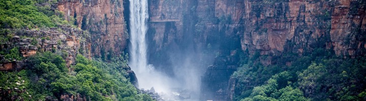 Waterval in Kakadu National Park die tussen hoge rotswanden in een groene kloof naar beneden stort.