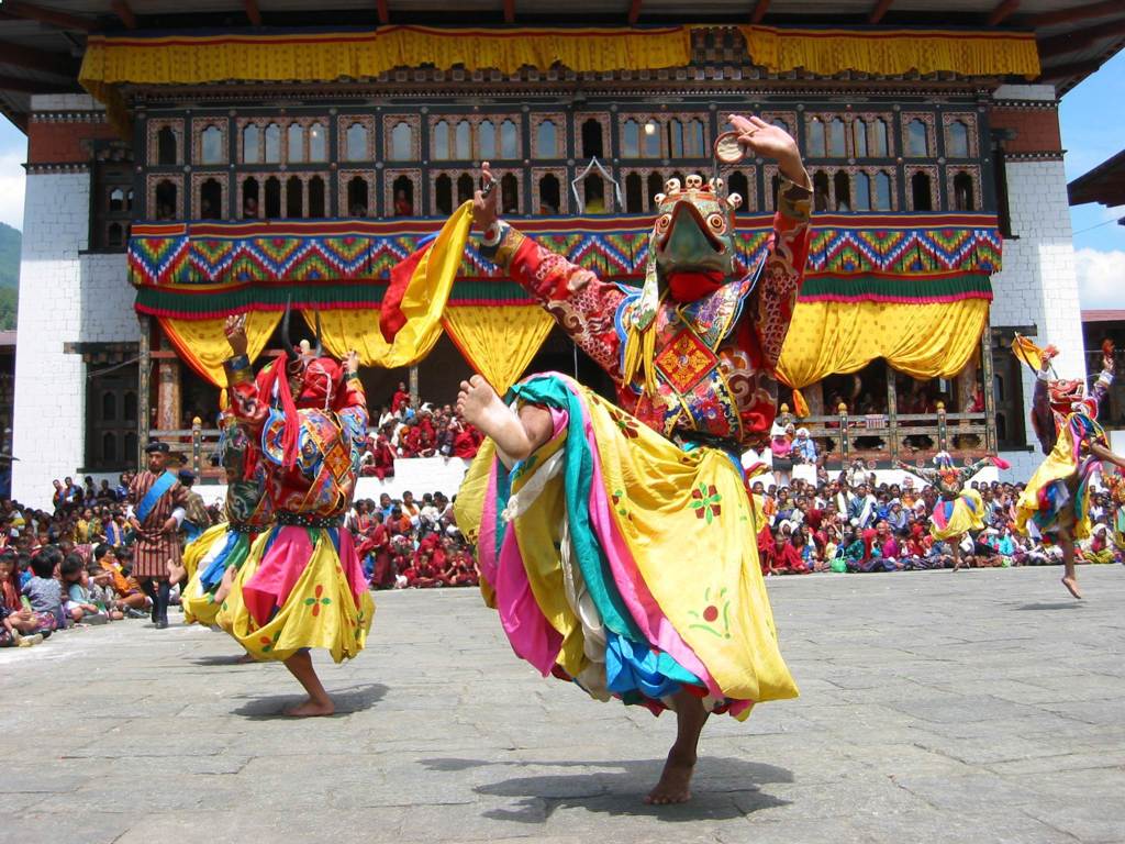 Gemaskerde dansers in kleurrijke kostuums tijdens een festival bij een Bhutanese dzong in de Himalaya.