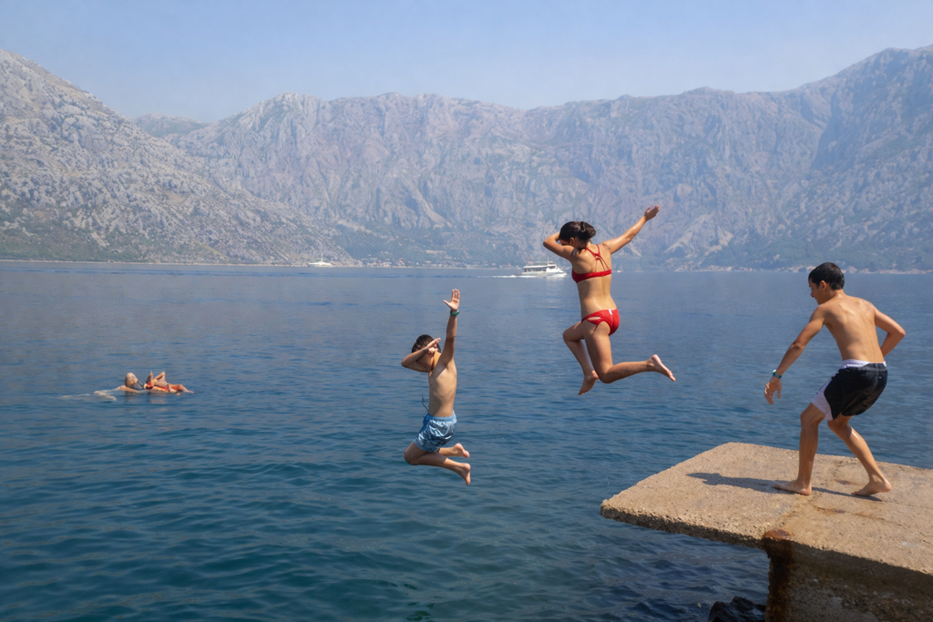 Kinderen springen vanaf een steiger in zee met bergen op de achtergrond in Kroatië en Montenegro.
