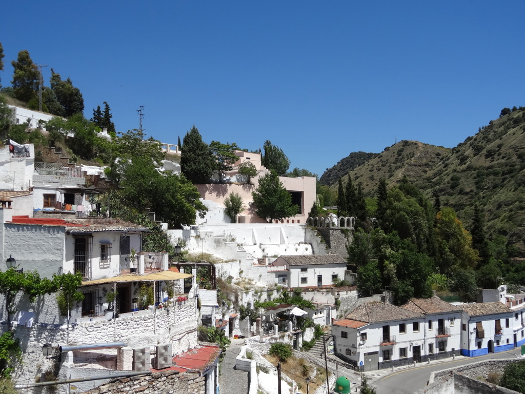 Witgekalkt bergdorp in Andalusië met huizen tegen de heuvel en groen dal onder een heldere blauwe lucht.