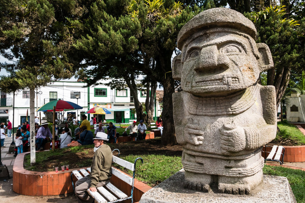 Steenbeeld in een park in Colombia, met mensen op bankjes en kleurrijke parasols op de achtergrond.