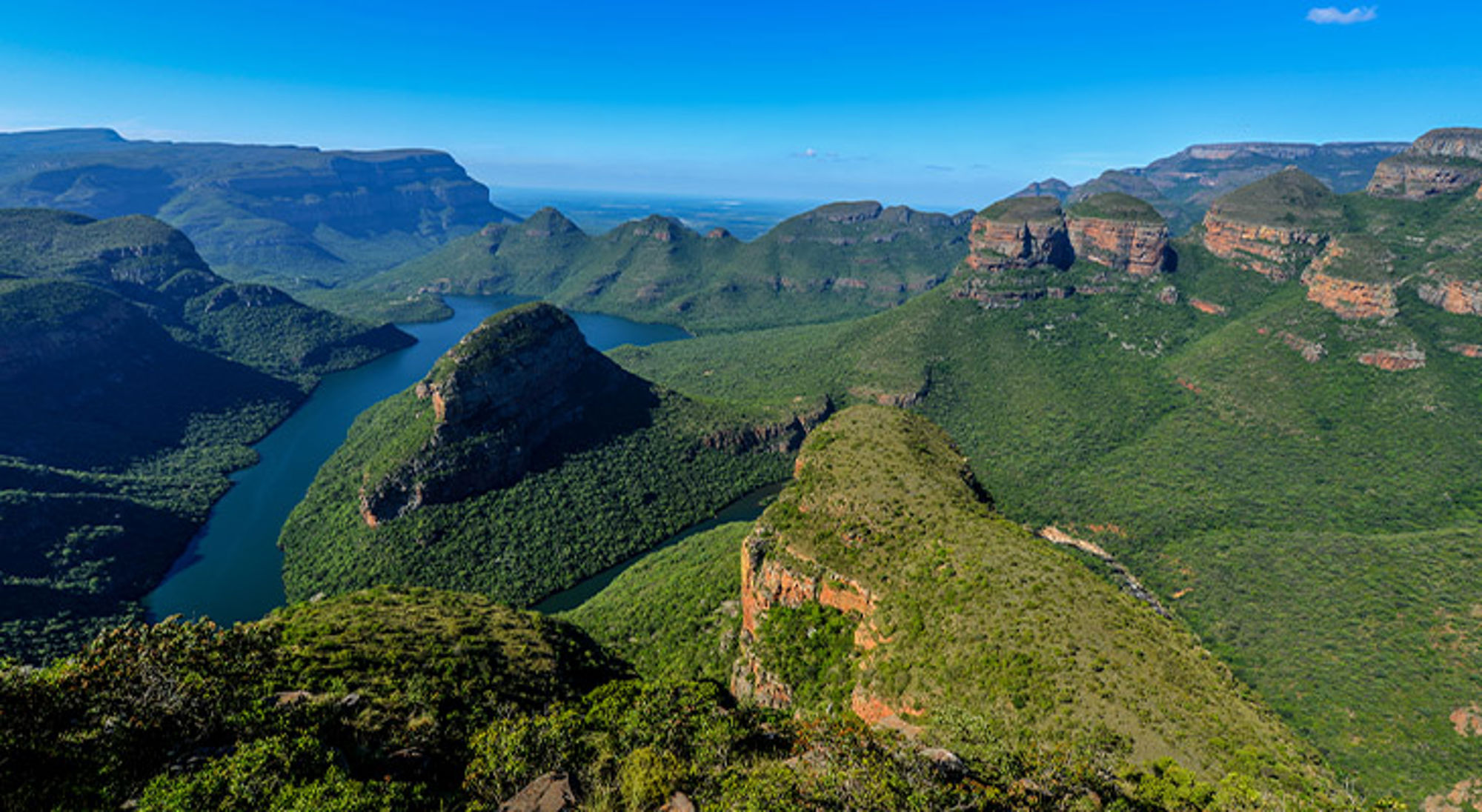 Blyde River Canyon Zuid-Afrika Panoramisch uitzicht op de Blyde River Canyon met groene bergen en kronkelende rivier onder een blauwe lucht.