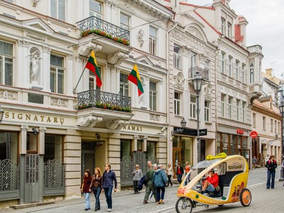 Straatbeeld in Vilnius met historische gevels, voetgangers en een fietstaxi voor Signatarų Namai.