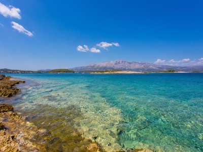 Heldere Adriatische zee bij de Kroatische kust, met rotsstrand en bergen op de achtergrond.