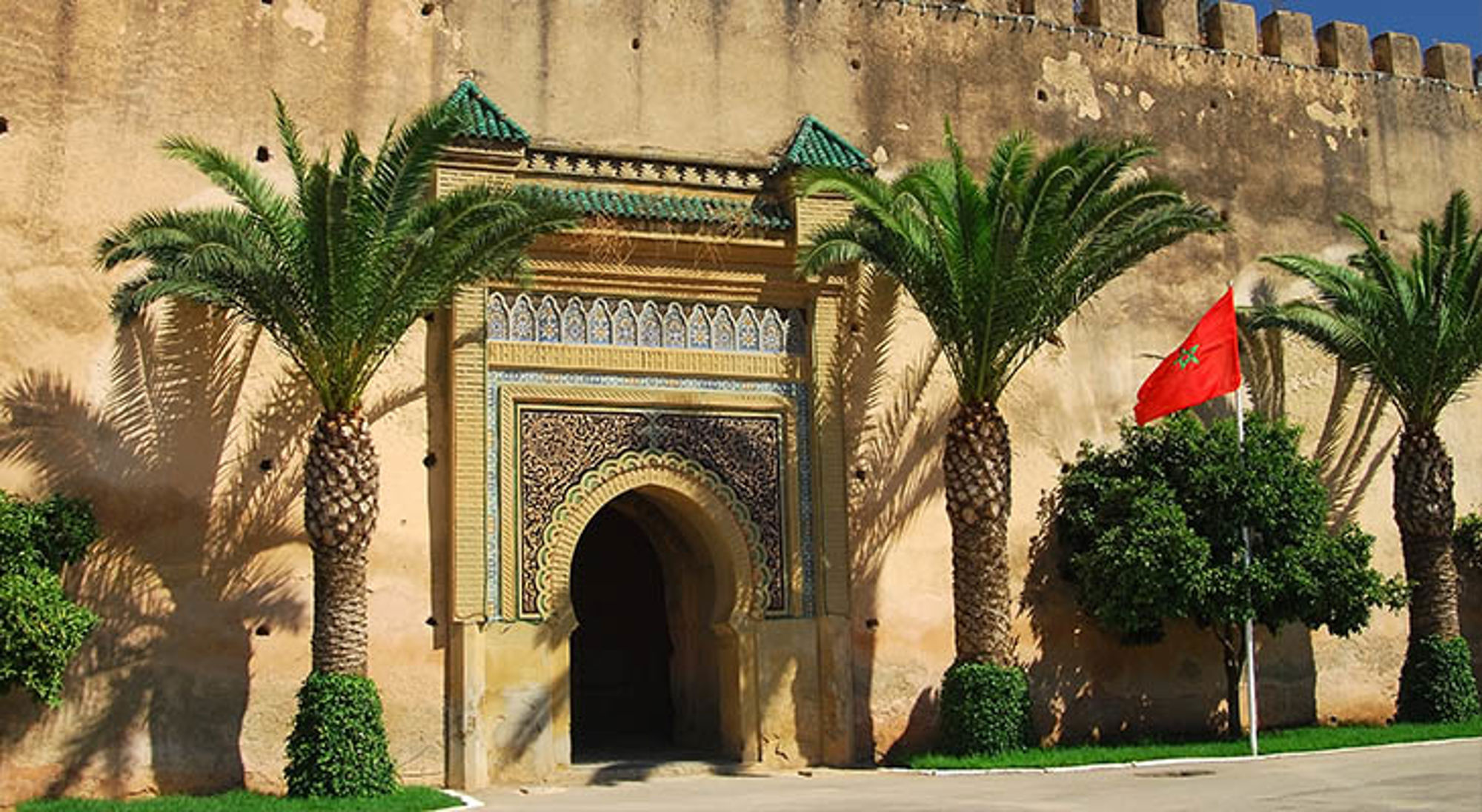 Meknes Versierde stadspoort in Marokko met palmboom en Marokkaanse vlag bij oude vestingmuur.