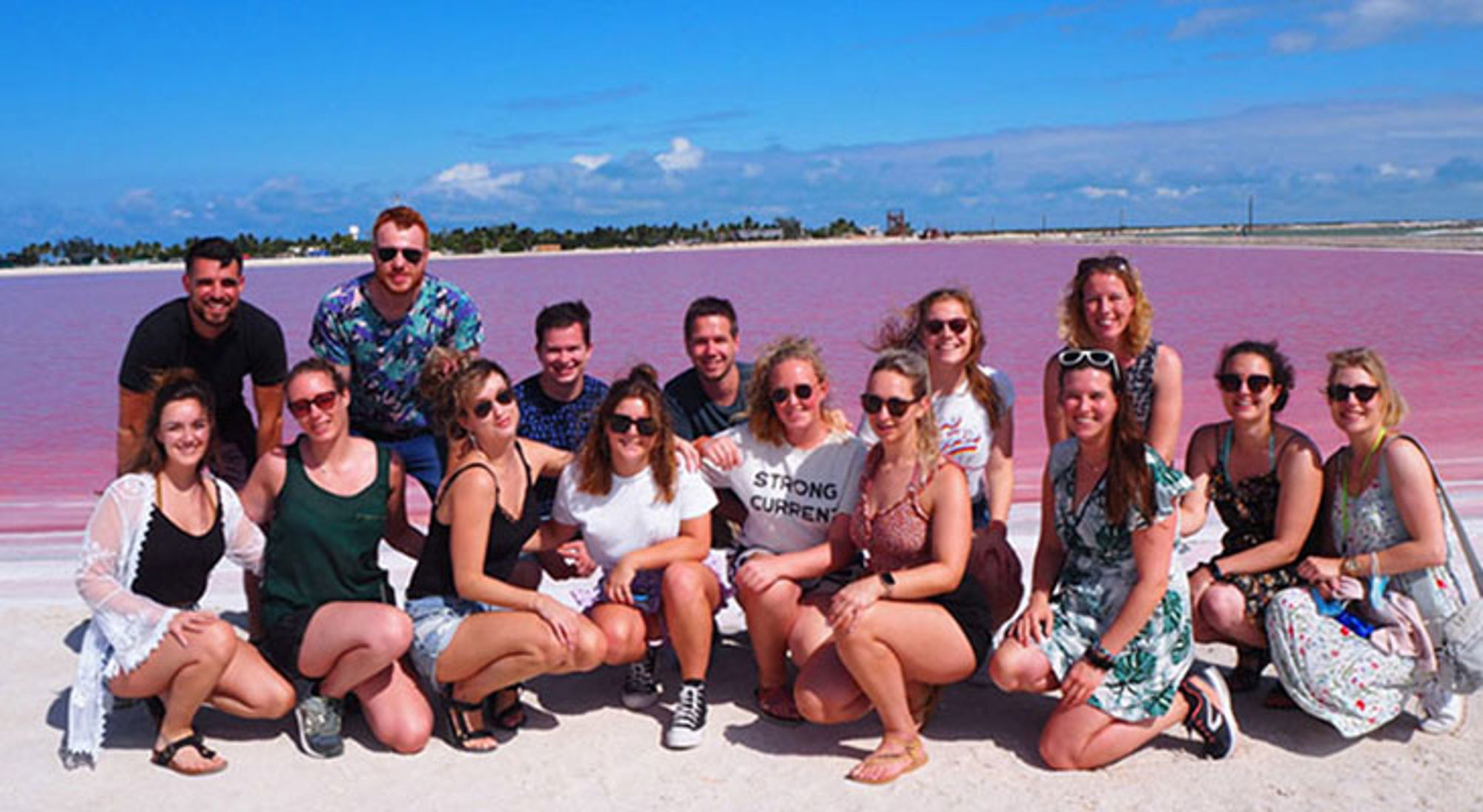 Groep reizigers poseert bij een roze zoutmeer onder een blauwe lucht.