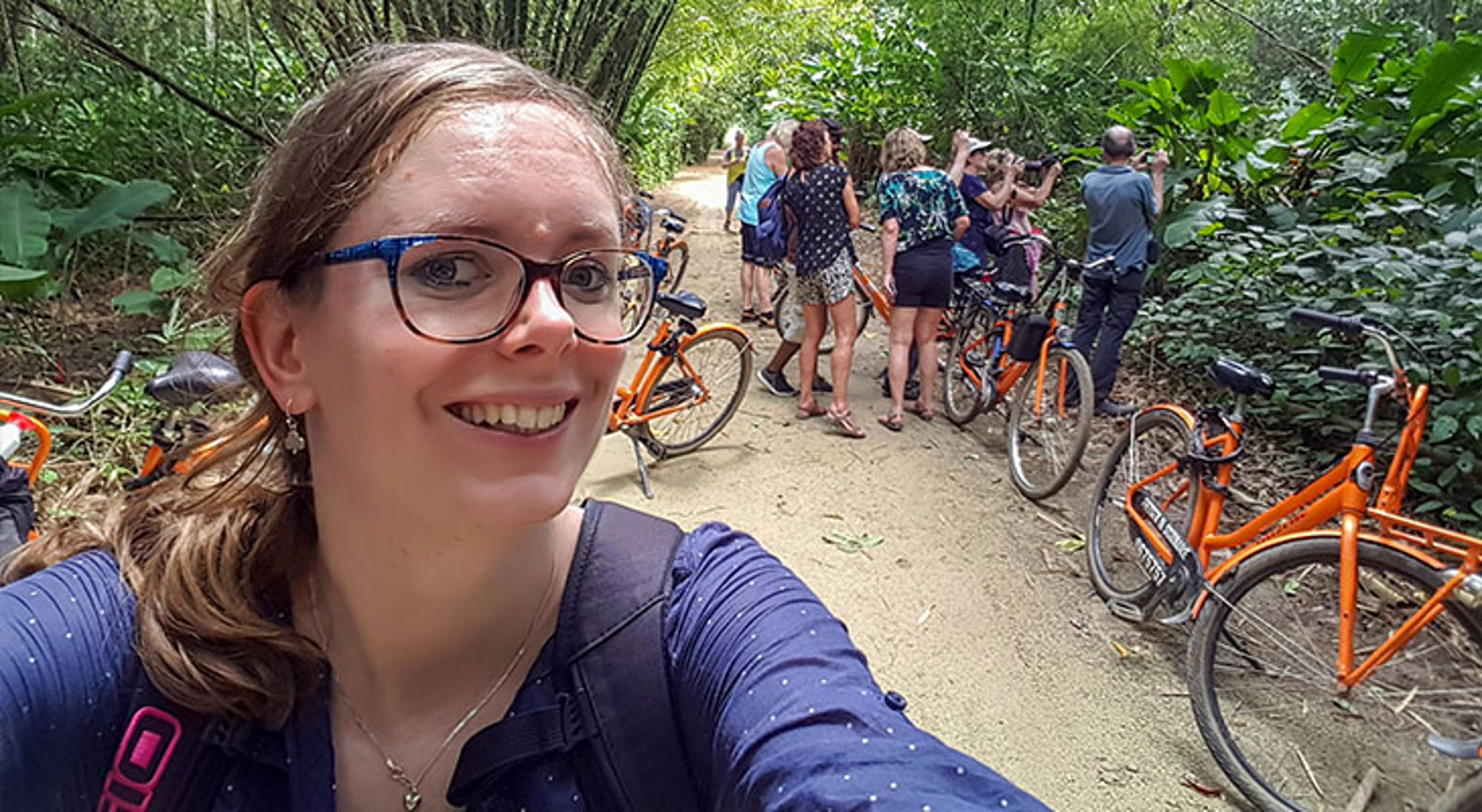 Commewijne district Suriname Fietstocht door een groen bos, met reizigers en oranje fietsen langs een zandpad.