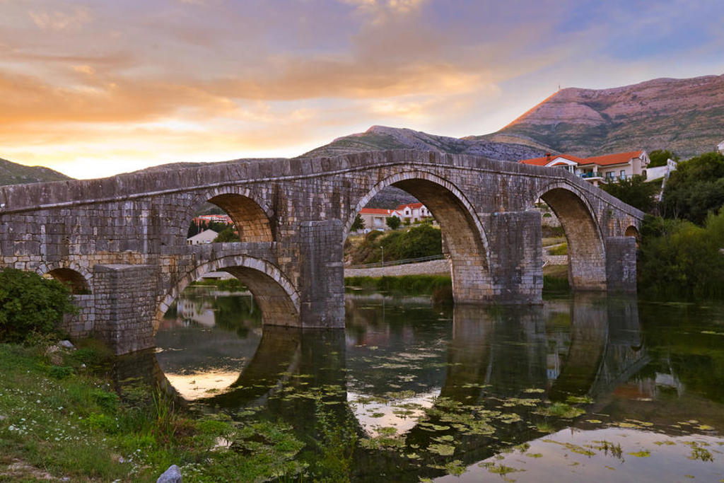 Oude stenen boogbrug over een rustige rivier bij zonsondergang in Montenegro.