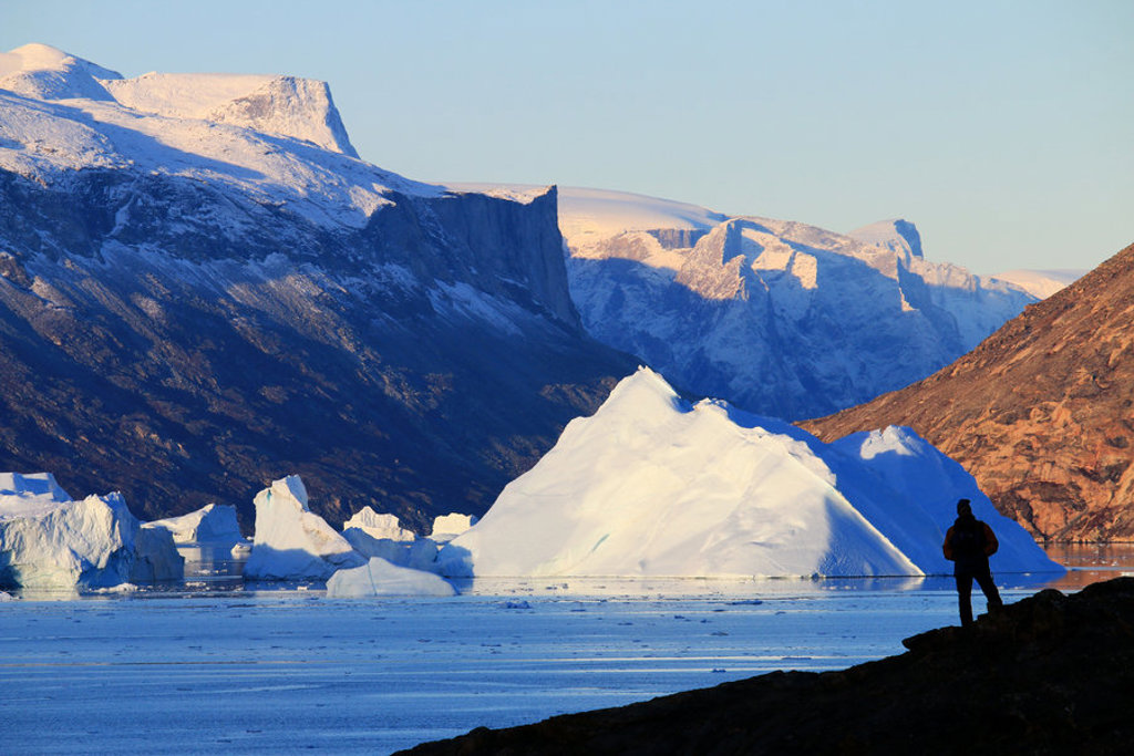 IJsbergen in een fjord met besneeuwde bergen in Groenland, met reiziger op de voorgrond.