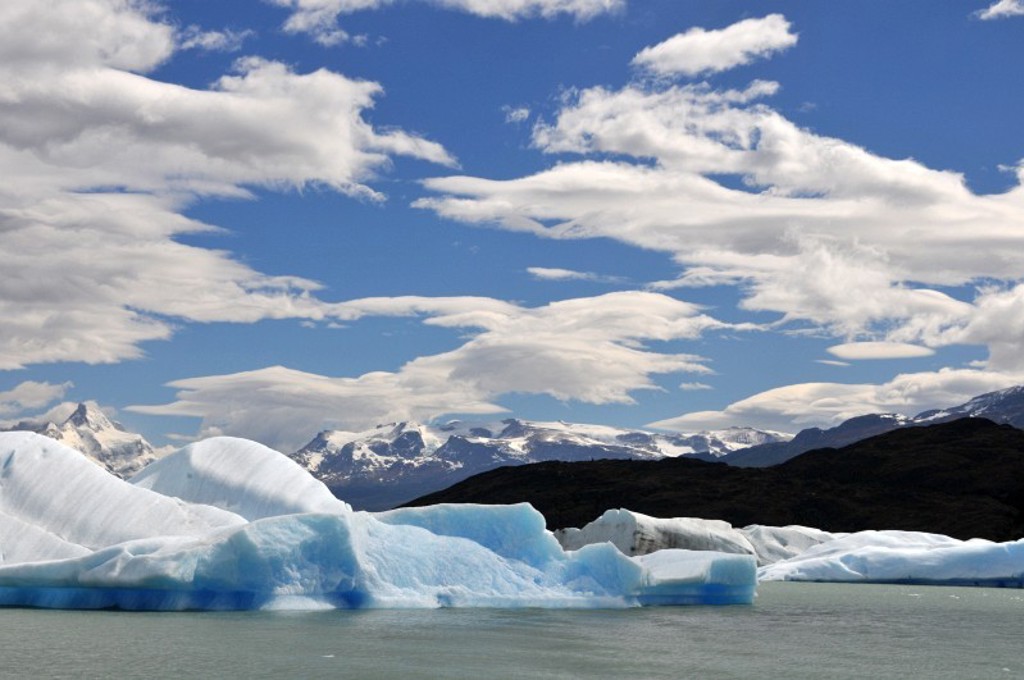 Blauwe ijsbergen in een Patagonisch meer met besneeuwde bergen onder een wolkenlucht, Argentinië.