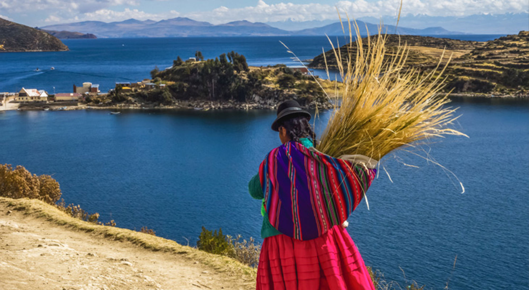 Vrouw in traditionele kleding met rietbundel op de oever van het Titicacameer in Bolivia.