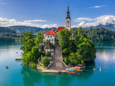 Kerk op het eiland in het Meer van Bled, Slovenië, met trappen naar de oever en boten op het water.