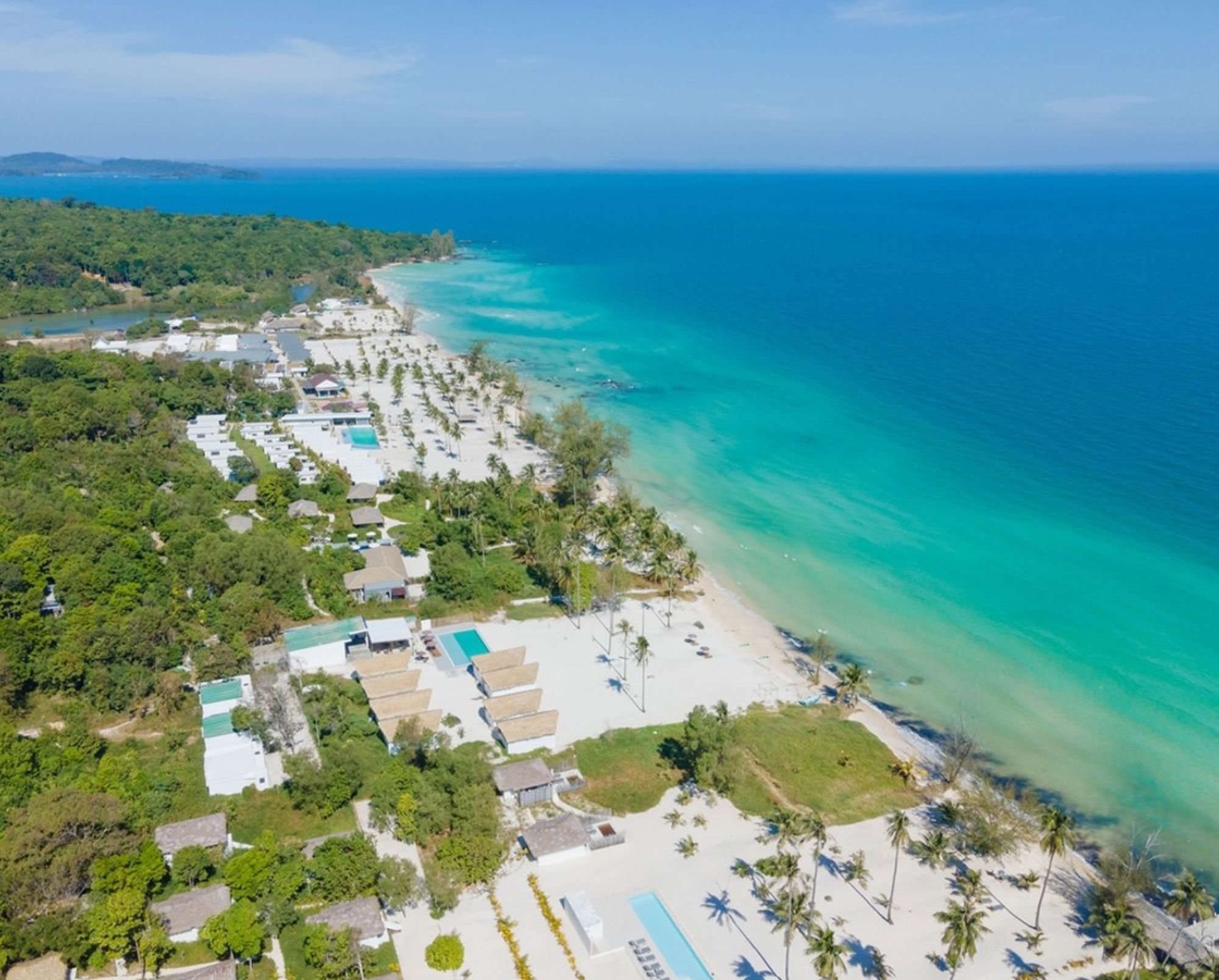 een wit zandstrand met palmbomen en helderblauw zeewater in Cambodja.