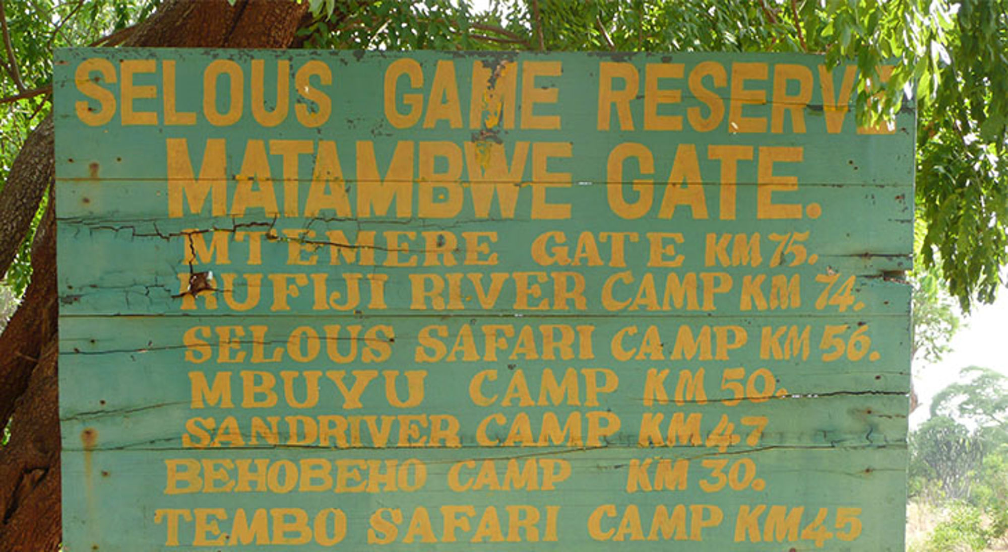 Houten wegwijzer bij Selous Game Reserve, Tanzania, met afstanden naar Matambwe Gate en safari camps.