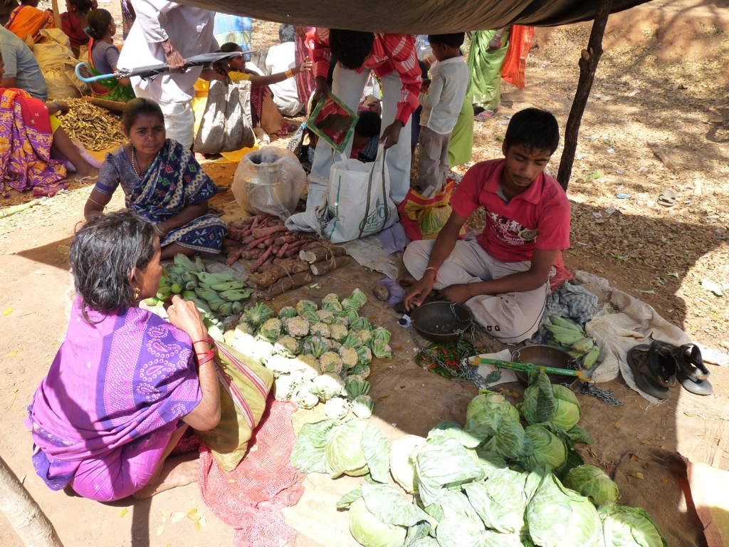 Groentemarkt in Orissa, India, met verkopers en verse groenten onder een afdak.