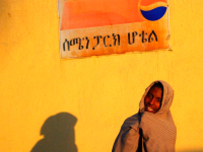 Ethiopische vrouw in traditionele omslagdoek bij een gele muur met Amhaars opschrift tijdens Route Ethiopië 29 dagen.