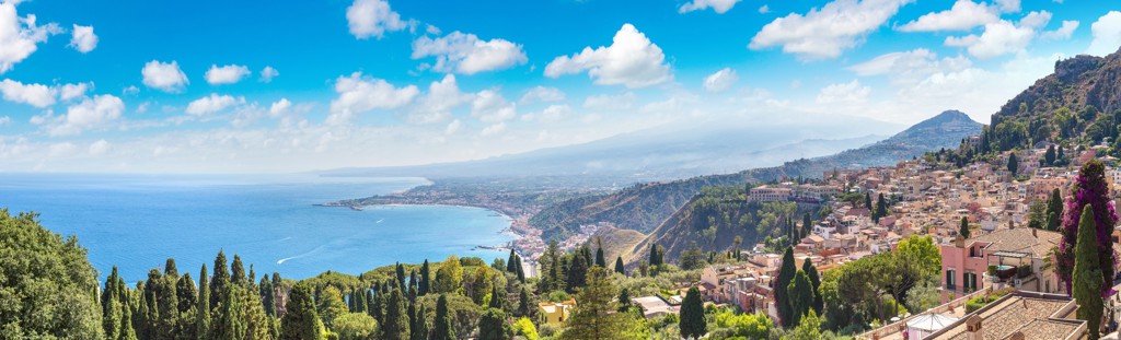 Panorama van Taormina aan de kust van Sicilië met azuurblauwe zee, heuvels en stad in de zon.