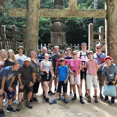 Groep reizigers tijdens een familiereis Japan bij een stenen torii-poort in een bosrijk tempelcomplex.