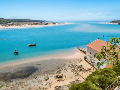 Uitzicht op de monding bij Alentejo en Algarve met strand, turkoois water, bootjes en wit huis met rood dak.