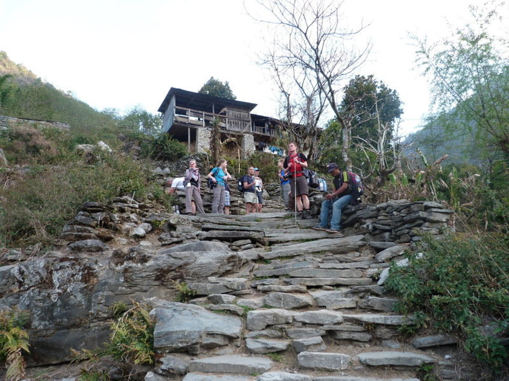 Groepsrondreis Nepal: wandelaars met rugzakken op een stenen bergpad langs een dorp.