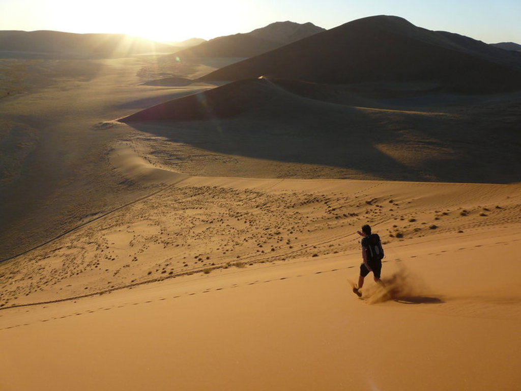 Reiziger loopt van een zandduin in Namibië bij zonsondergang tijdens een groepsrondreis met lodge/hotel.
