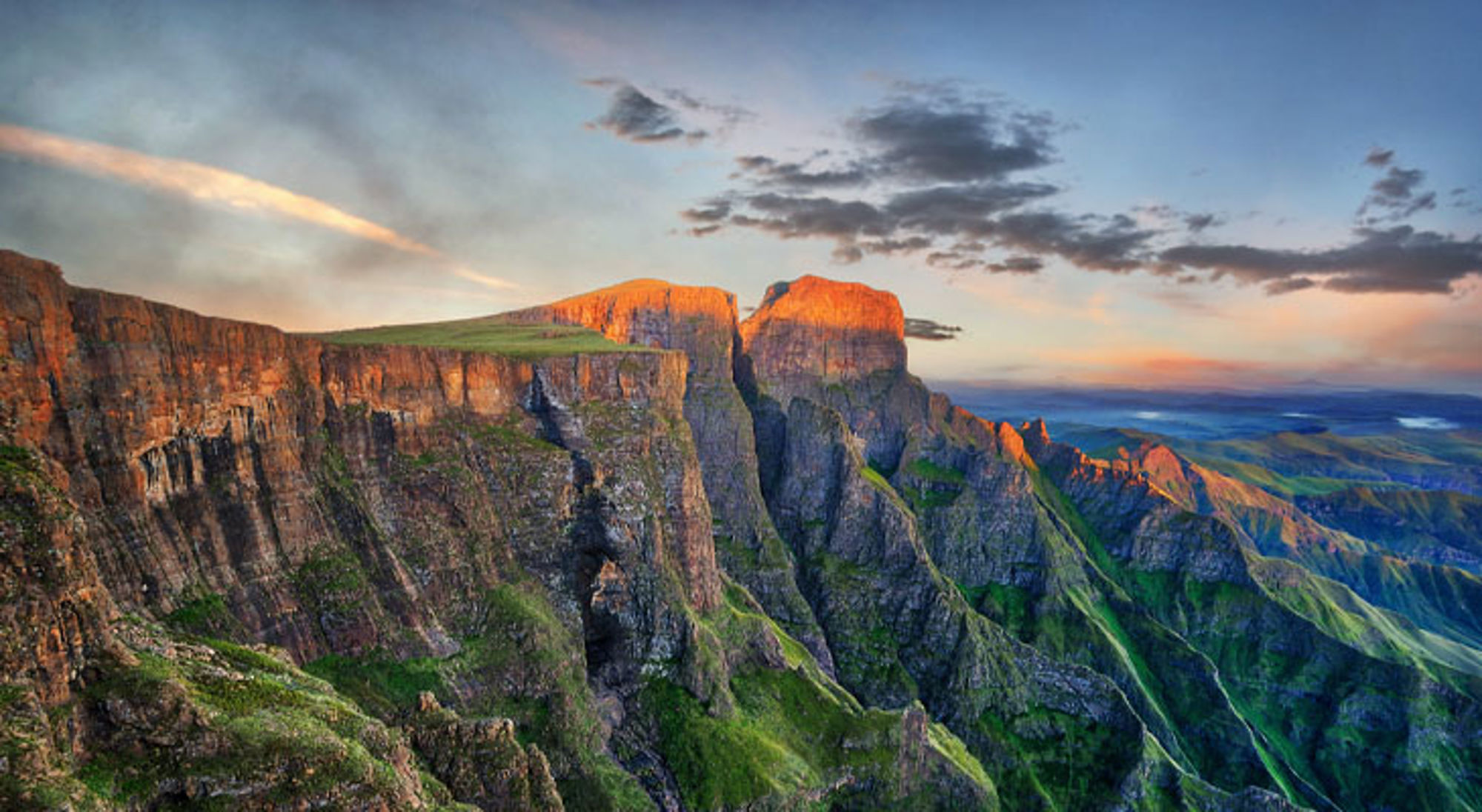 Uitzicht op de Drakensbergen met steile kliffen en groene valleien bij zonsondergang in Zuid-Afrika.