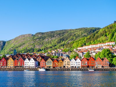 Gekleurde houten huizen aan de Bryggen-kade in Bergen, Noorwegen, met groene bergen op de achtergrond.