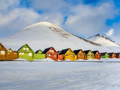Kleurrijke houten huizen in Longyearbyen op Spitsbergen, met besneeuwde berg op de achtergrond.