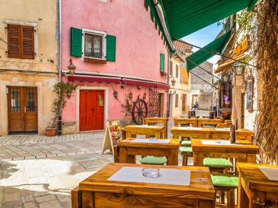 Terras met houten tafels in een smalle straat met kleurrijke huizen in Rovinj, Kroatië.