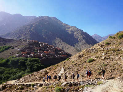 Wandelaars op bergpad in het Atlasgebergte met dorp op de helling tijdens de route naar Mt. Toubkal.