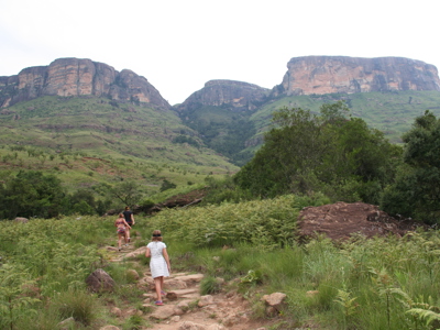 Wandelaars op een pad door groen heuvelgebied met rotsplateaus tijdens de Route Zuid-Afrika.