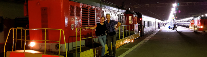 Reizigers poseren bij de Trans-Siberië Express op een verlicht station in de avond.