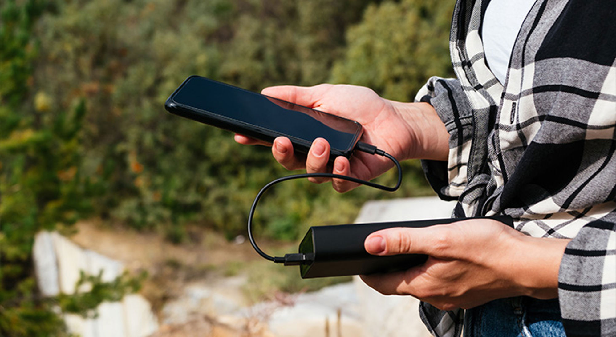 Powerbank Handen houden een smartphone vast die via een kabel is verbonden met een powerbank.
