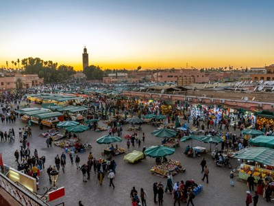 Jemaa el-Fna plein in Marrakech bij zonsondergang, met drukke markt en minaret op de achtergrond.
