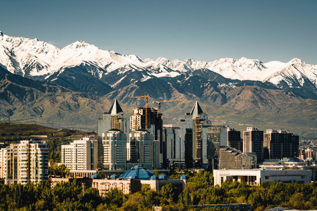 Skyline van Almaty met op de achtergrond de besneeuwde Tian Shan-bergen tijdens de Zijderoute treinreis.