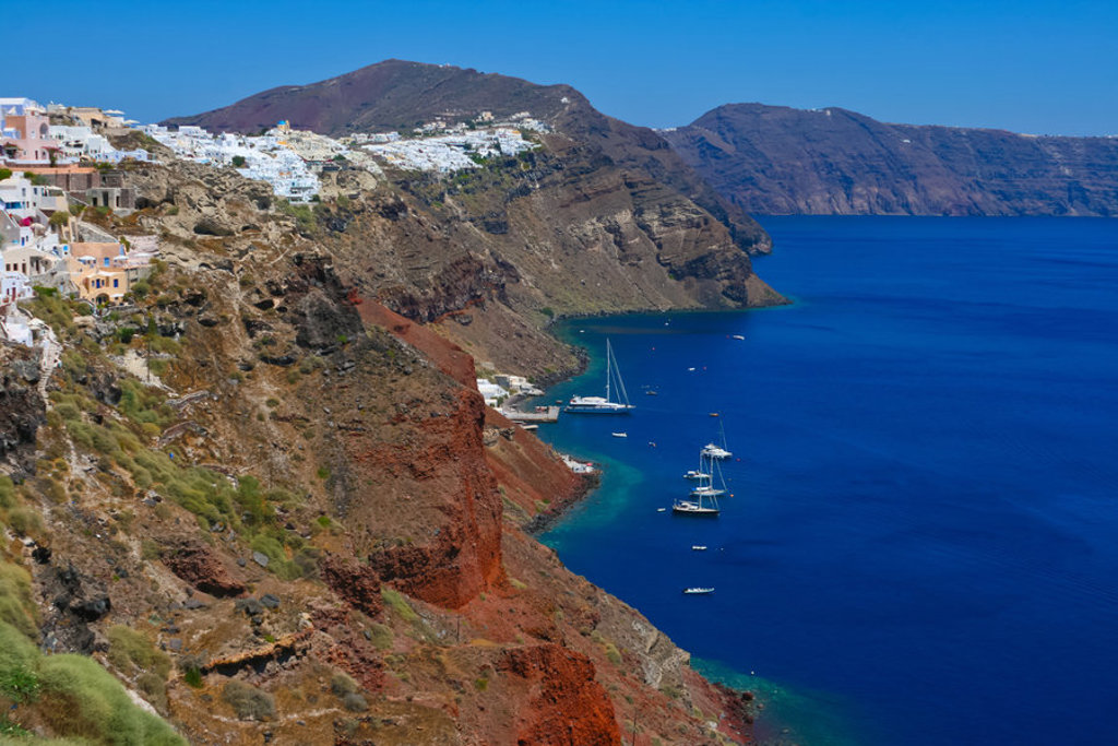 Kustlijn met witte huizen op de kliffen van Santorini, met zeilboten in de caldera, Griekenland.